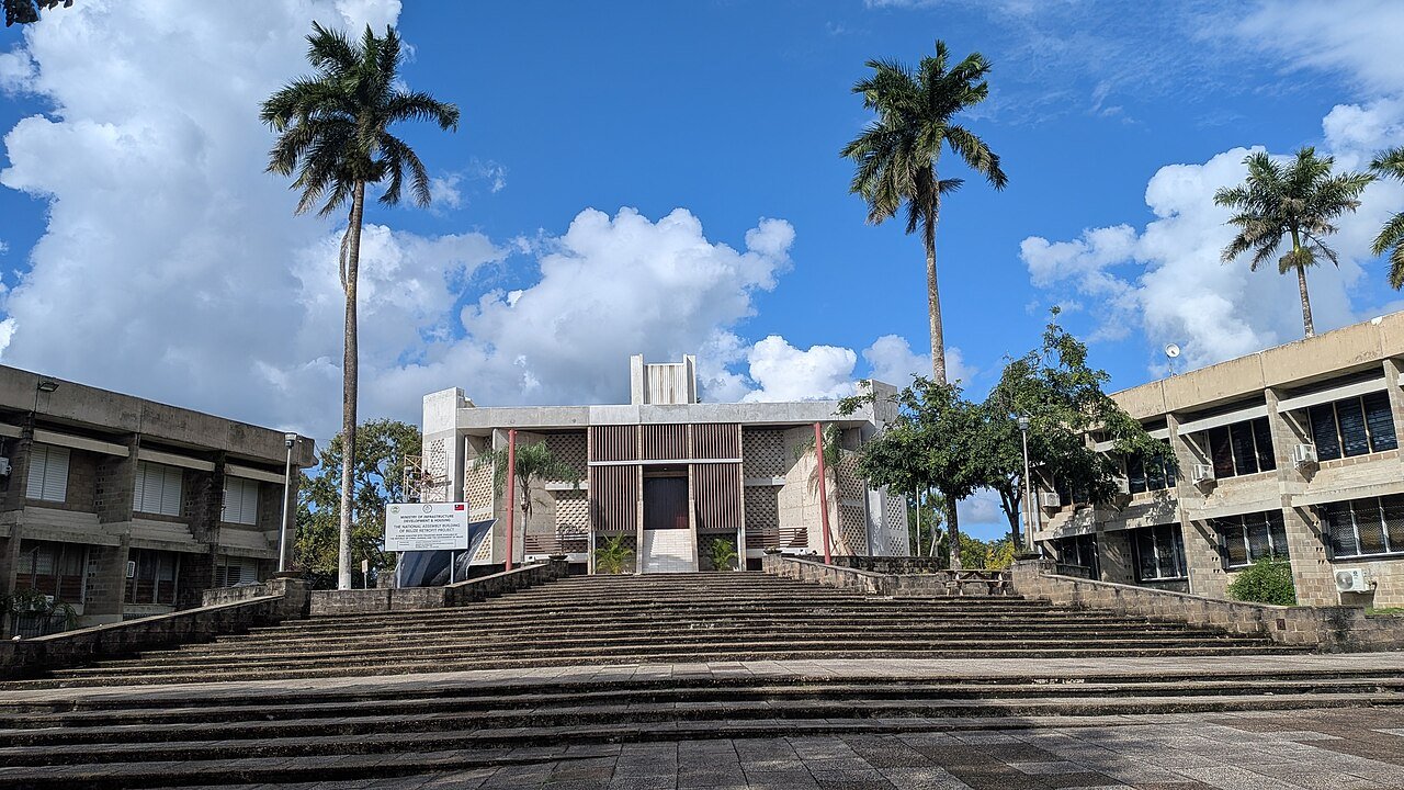 Fachada de la Asamblea Nacional de Belice en Belmopán, con escalinata y palmeras, en diciembre de 2025.